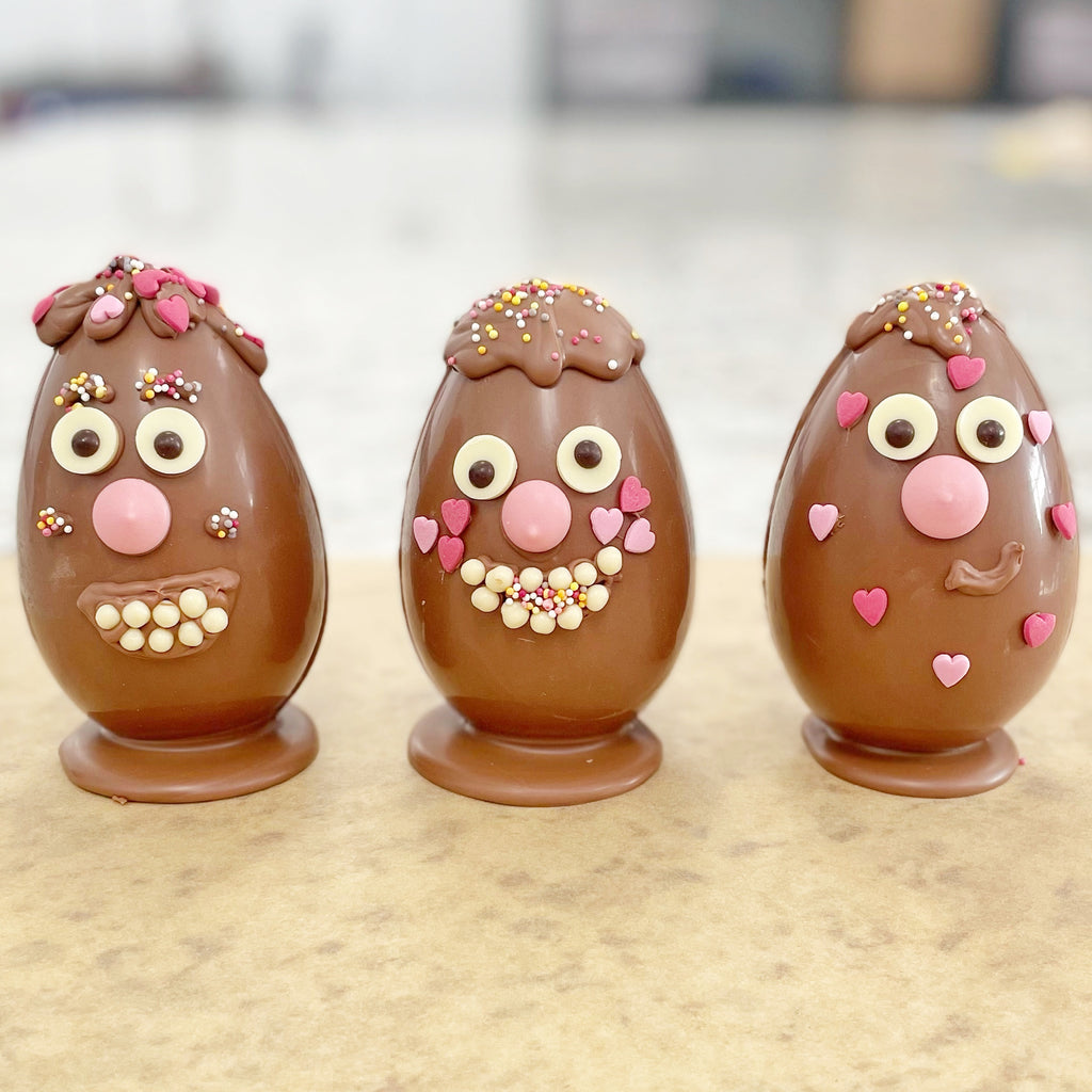 a woman holding a chocolate easter egg that has been decorated with a smiley face. 