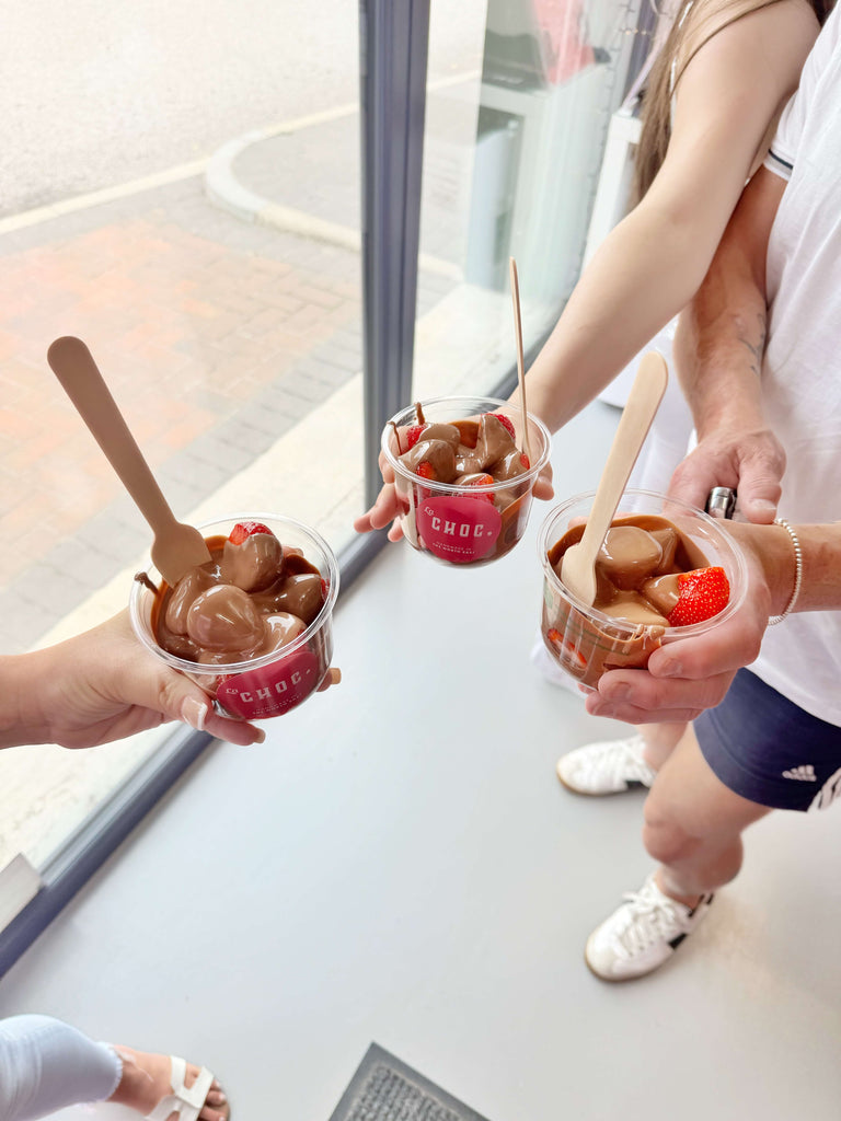 Three people holding clear pots of milk chocolate covered strawberries at La Chocolatrice in Coxhoe, Durham, North East England
