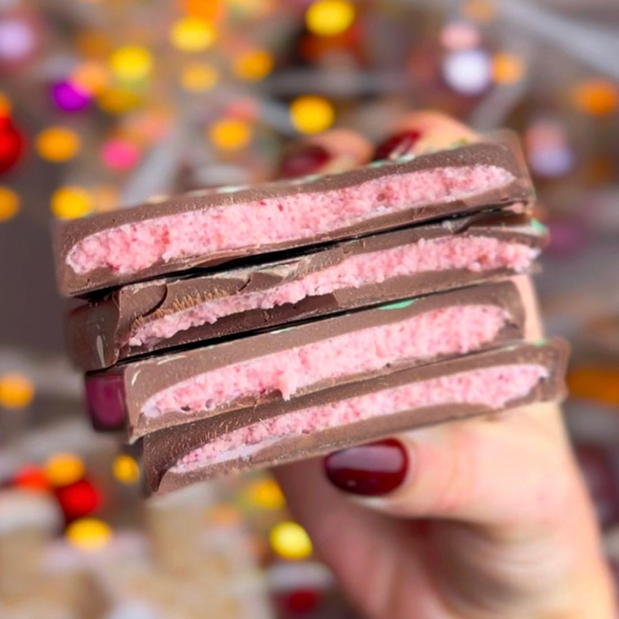 A milk chocolate bar, snapped in two, revealing a pink strawberry ganache centre. 