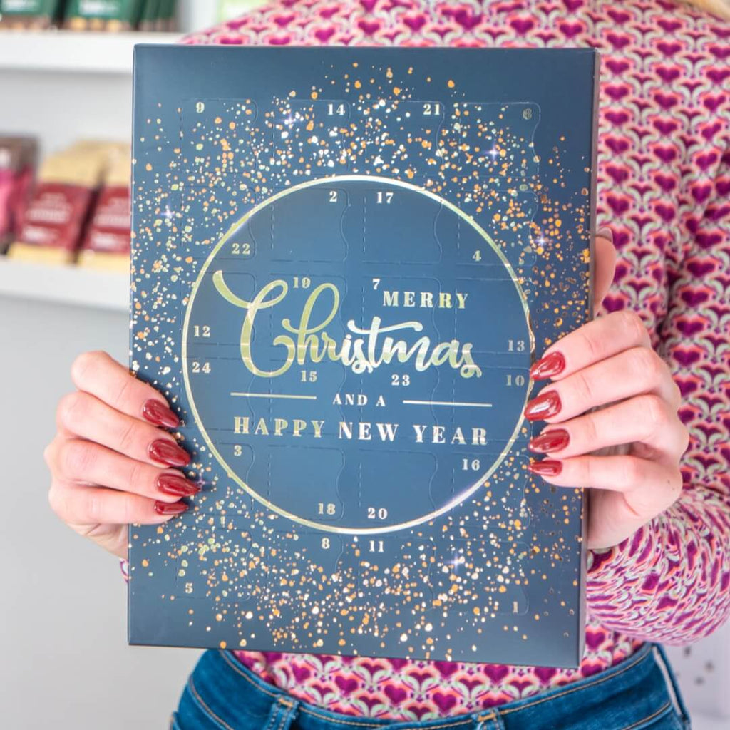 Person holding a 'Merry Christmas and Happy New Year' advent calendar, showcasing the design for the advent calendar making workshop at La Chocolatrice.