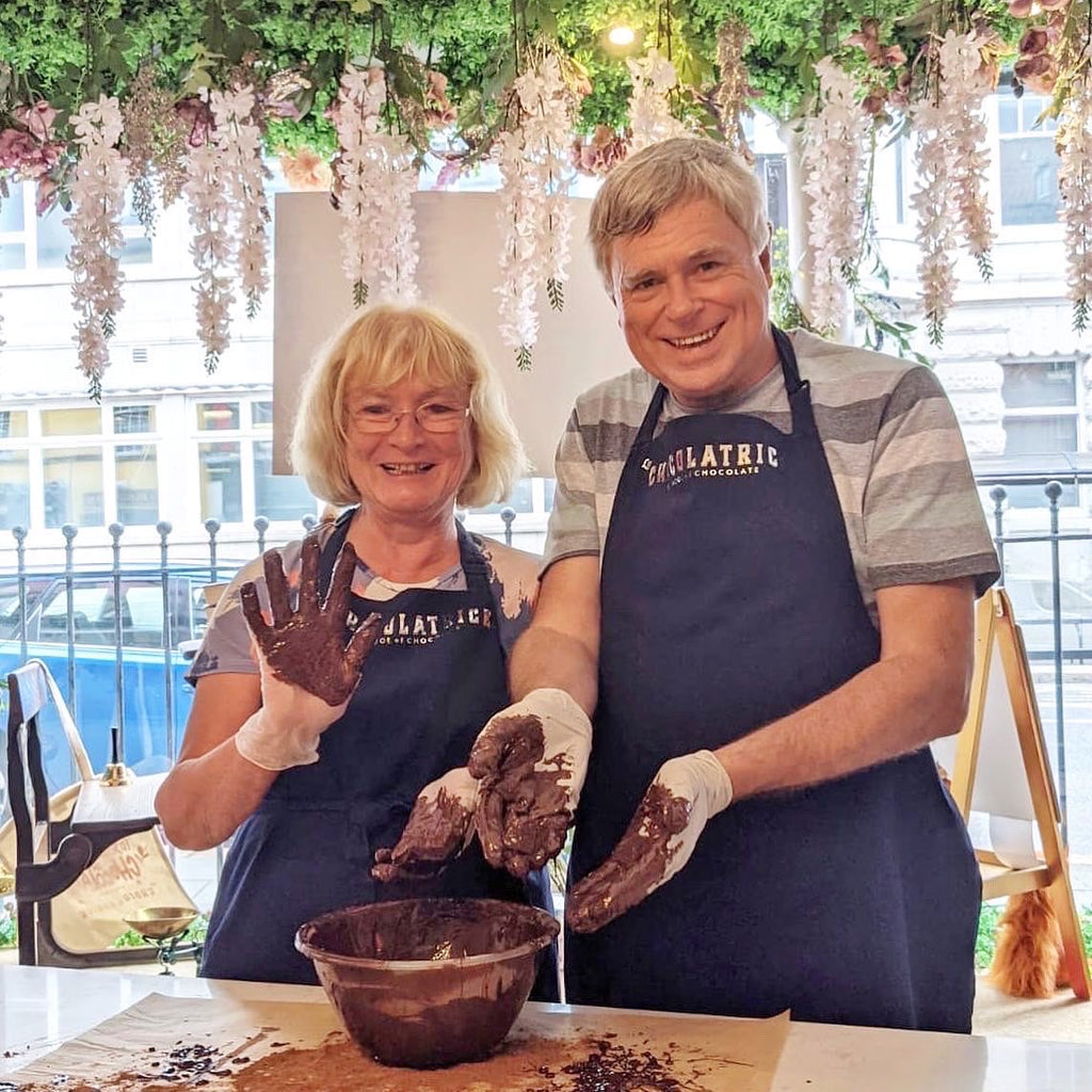 Couple enjoying a hands-on chocolate making workshop at La Chocolatrice in County Durham, smiling with chocolate-covered hands.