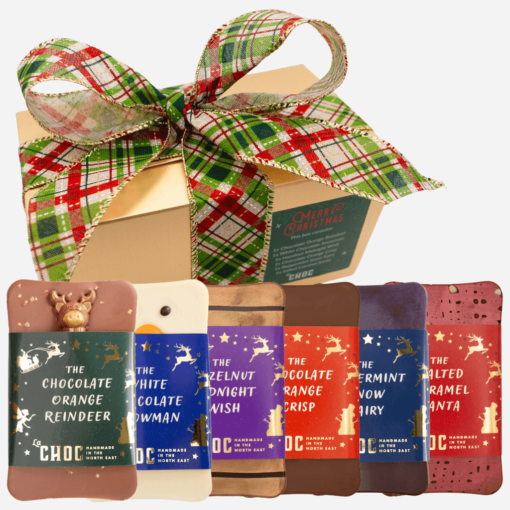 A festive gold gift box tied with a red and green plaid ribbon sits behind six handmade, Christmas-themed chocolate bars. The chocolate bars are individually wrapped with labels like "The Chocolate Orange Reindeer," "The White Chocolate Snowman," "Hazelnut Midnight Wish," "Chocolate Orange Crisp," "Peppermint Snow Fairy," and "Salted Caramel Santa."