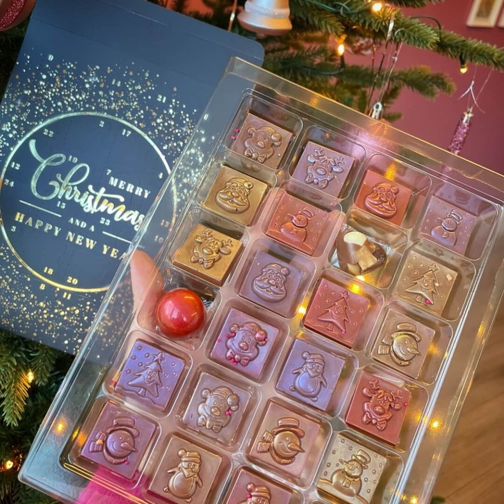 An open advent calendar showing various festive chocolate pieces, with a Christmas tree in the background.