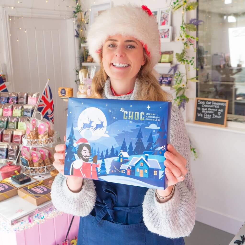 La Chocolatrice founder smiling and holding the Christmas advent calendar inside the Durham chocolate shop.