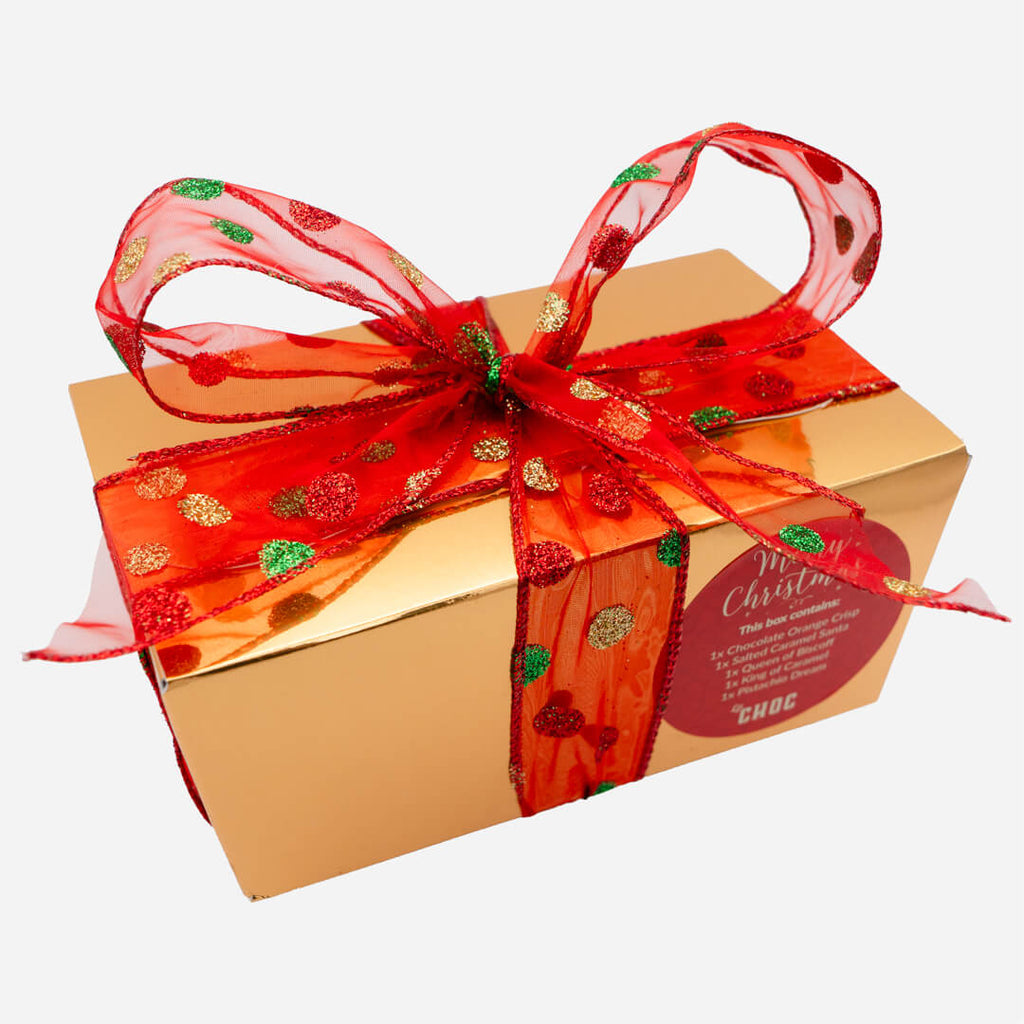Gold Christmas chocolate gift box from La Chocolatrice with red ribbon decorated with green and gold glitter dots.