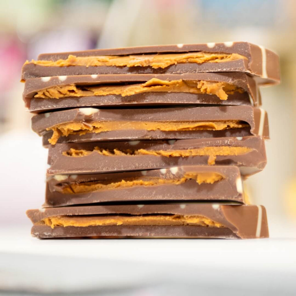 A stack of The Queen of Biscoff chocolate bars from La Chocolatrice, featuring layers of creamy milk chocolate filled with a generous amount of Biscoff spread, offering a rich and indulgent treat.