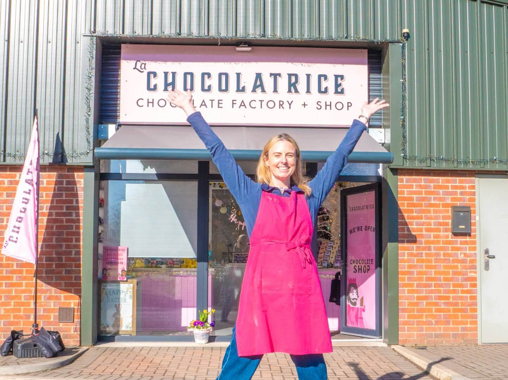 Zoe from La Chocolatrice outside the Chocolate Factory and Shop in the North East, wearing a pink apron and smiling.